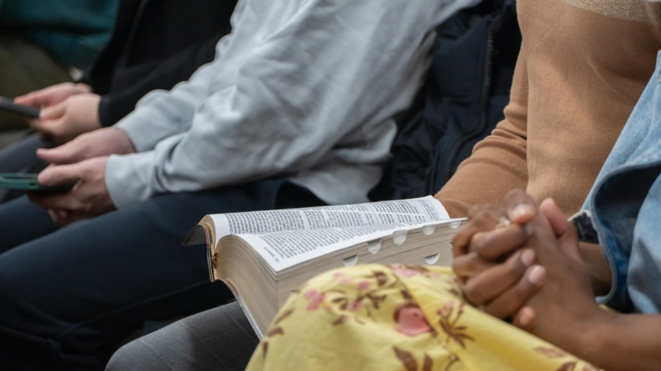 People sitting with open bible and clasped hands